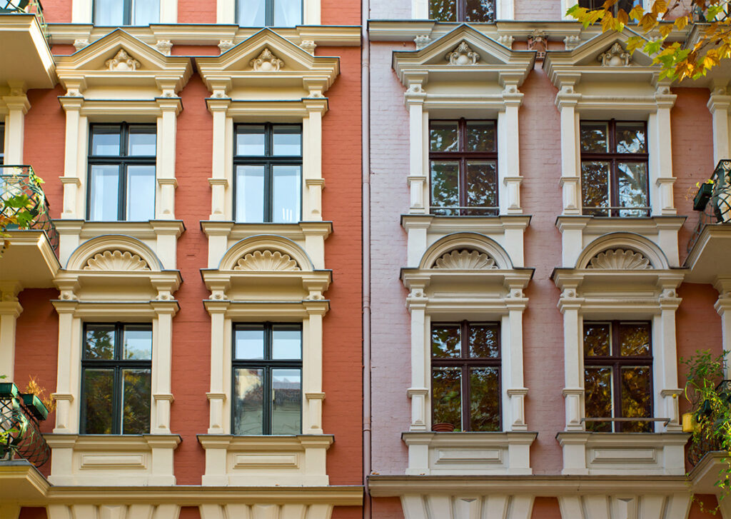 Fenster mit Stuck an der Fassade von 2 Häusern in orangener und rosaner Farbe